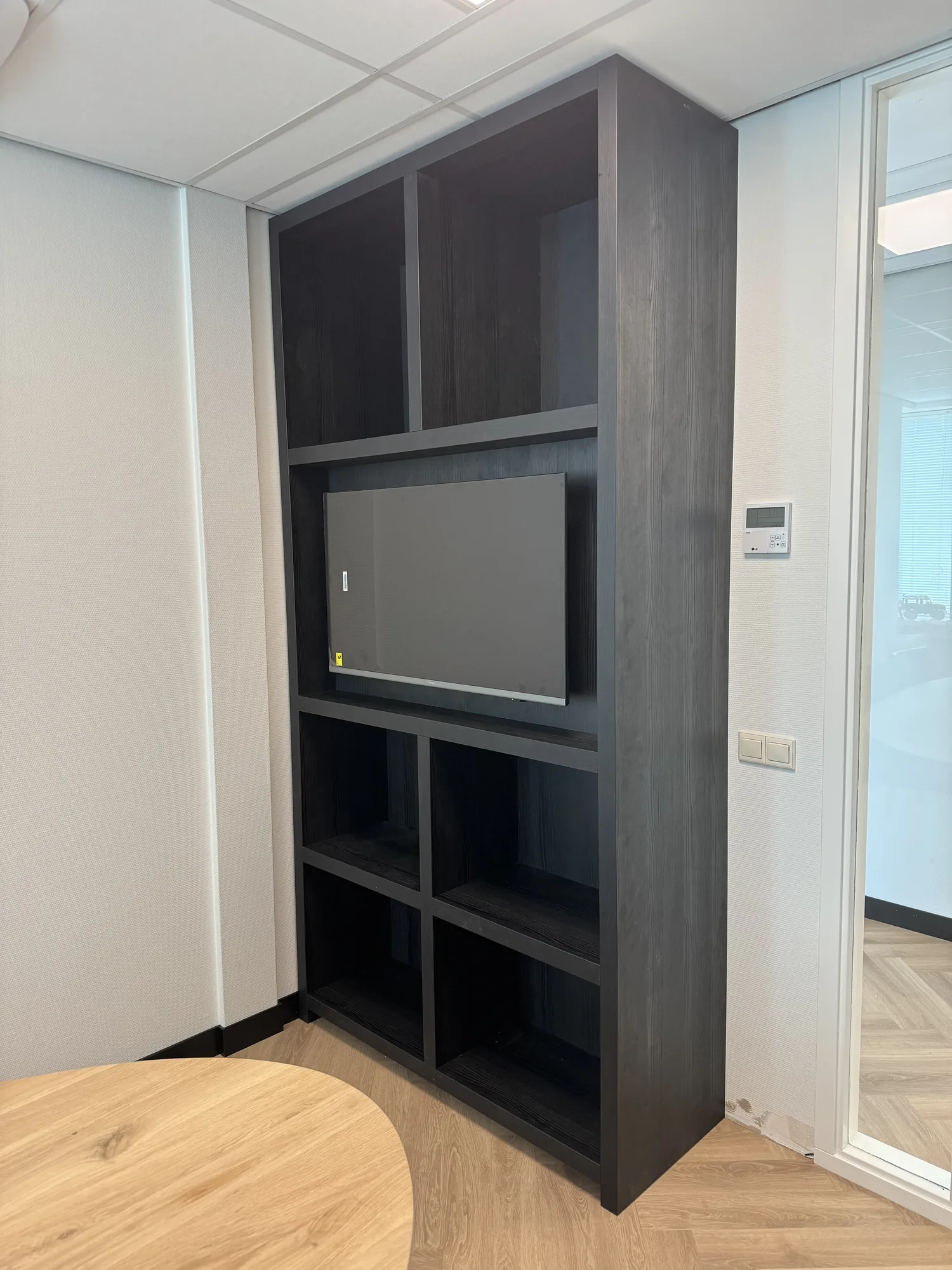 Zwarte kast met open vakken en een scherm in het midden, in een kantoor