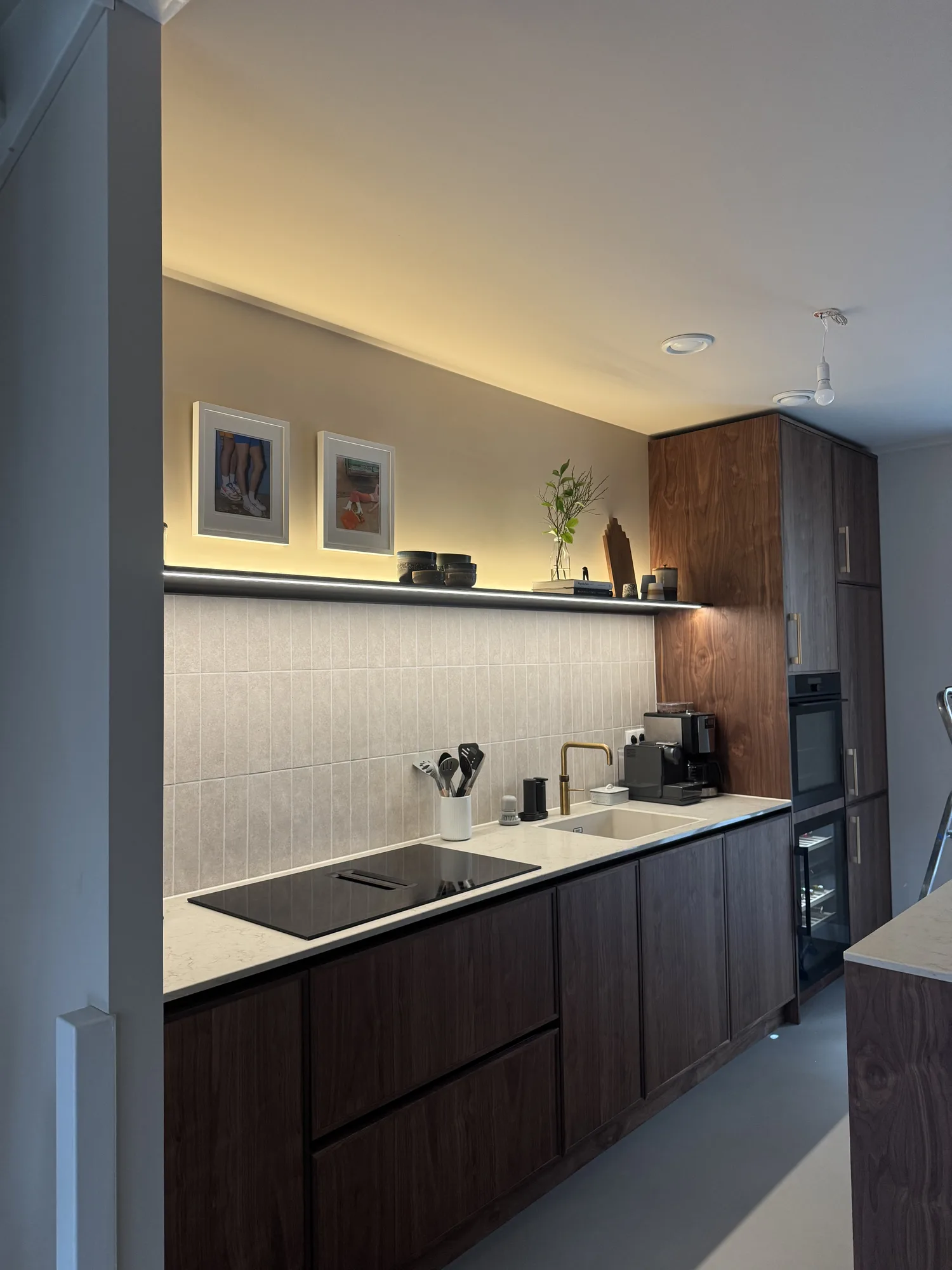 Keukenwand in donker noten met een licht werkblad, een verlicht schap en een hoge kast met oven