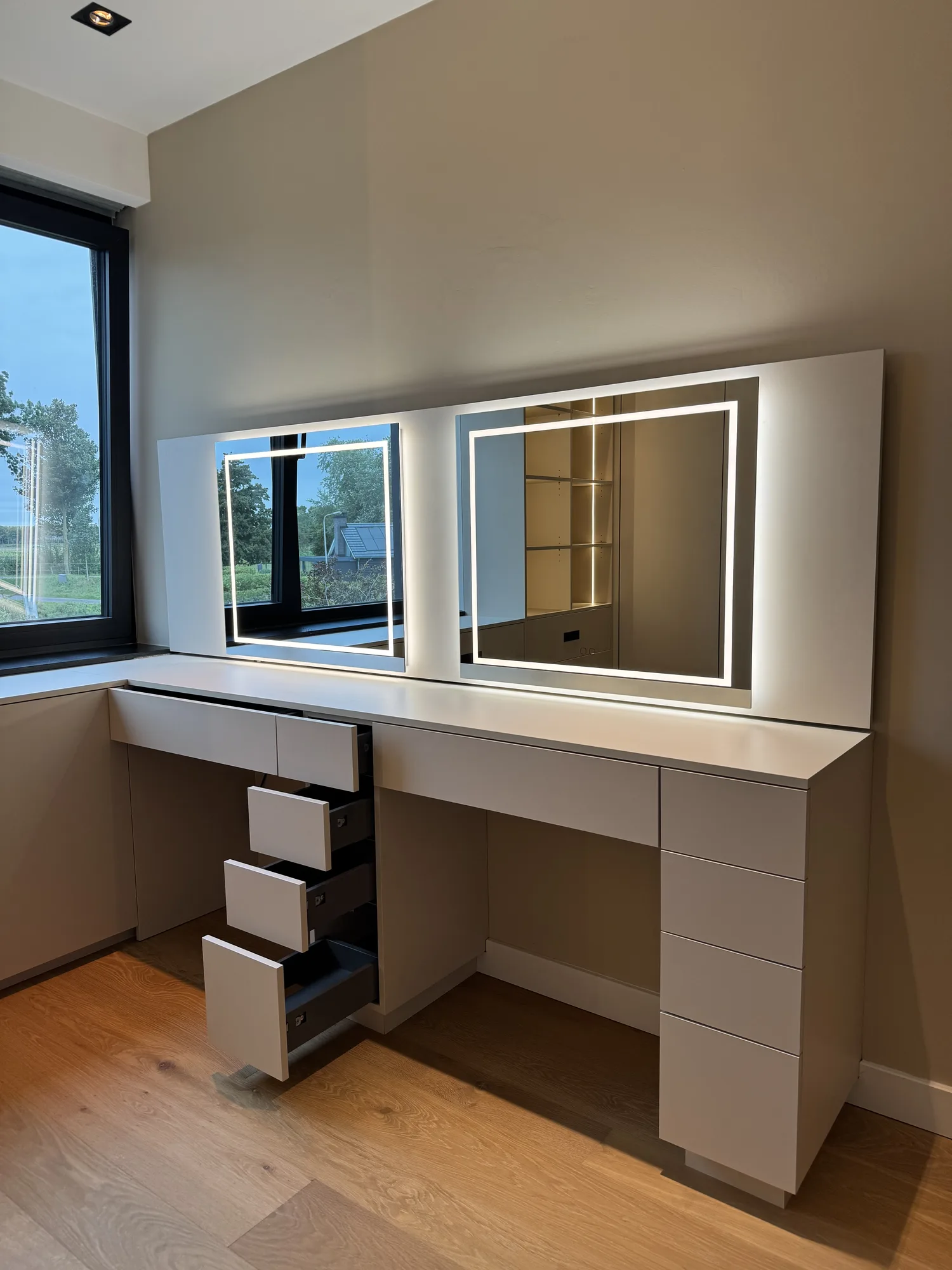 Kaptafel met twee verlichte spiegels en laden, onder het raam van de kleedkamer