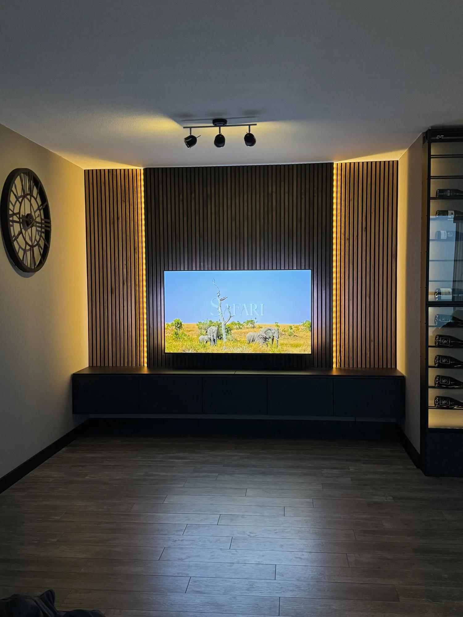 Tv-wand met verticale houten lamellen, verlichting erachter en een zwart laag meubel eronder