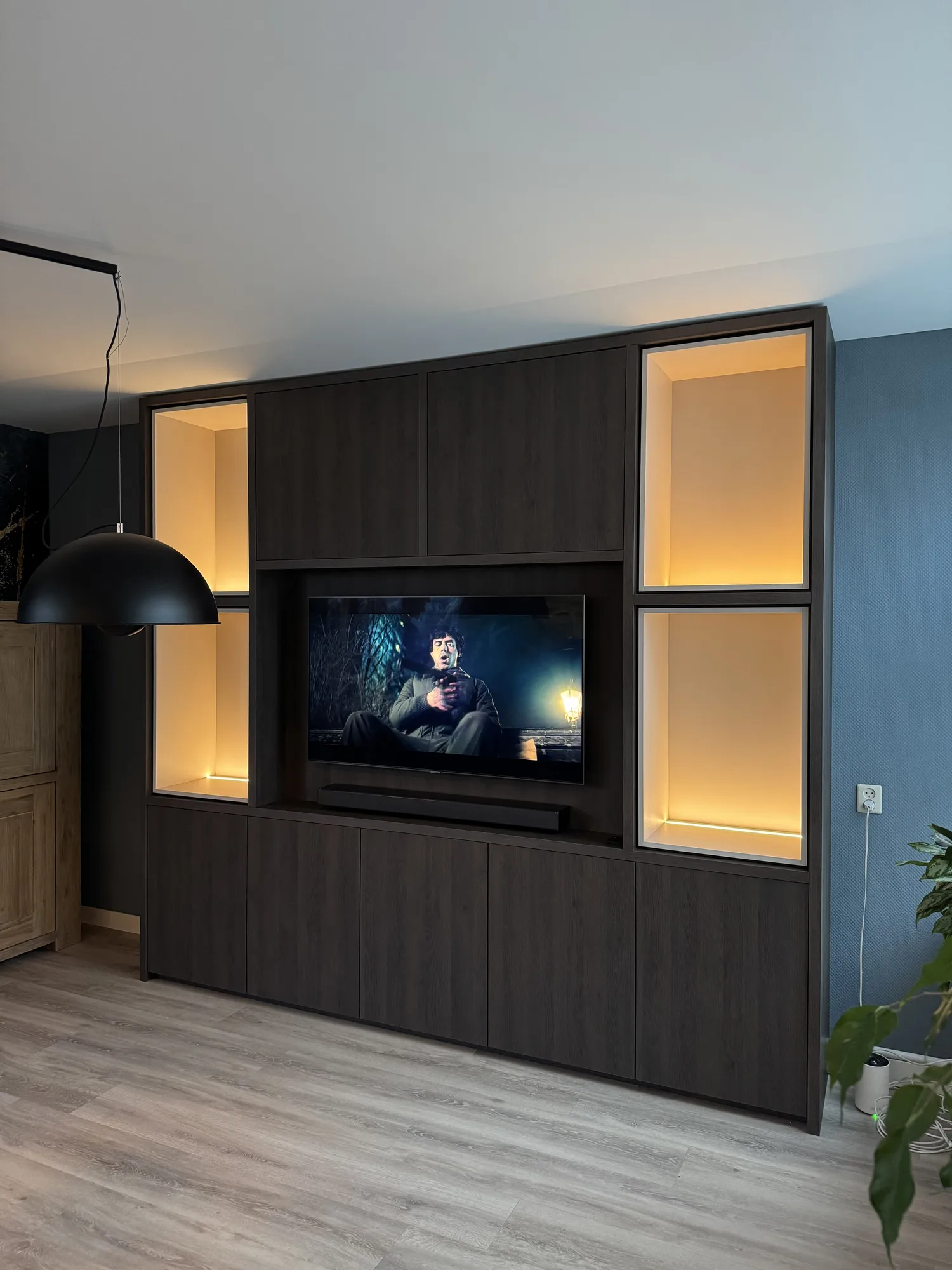 Donkere tv-wand met verlichte vitrines naast het scherm en kasten eronder