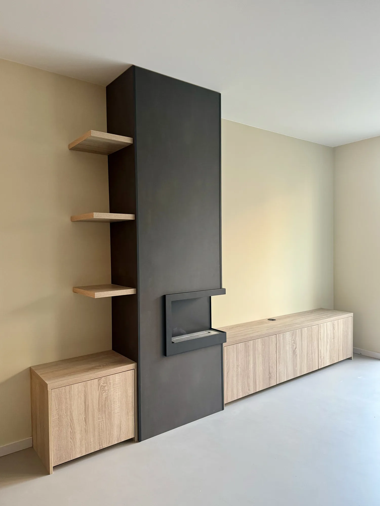 Donkere wand met een haard, zwevende schappen in eiken en een laag meubel in eiken