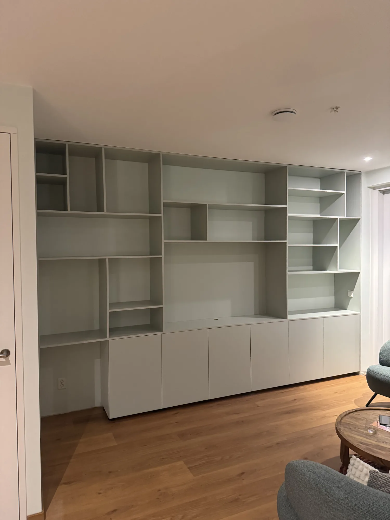 Wandkast in saliegroen met open vakken boven en deuren onder, in de woonkamer