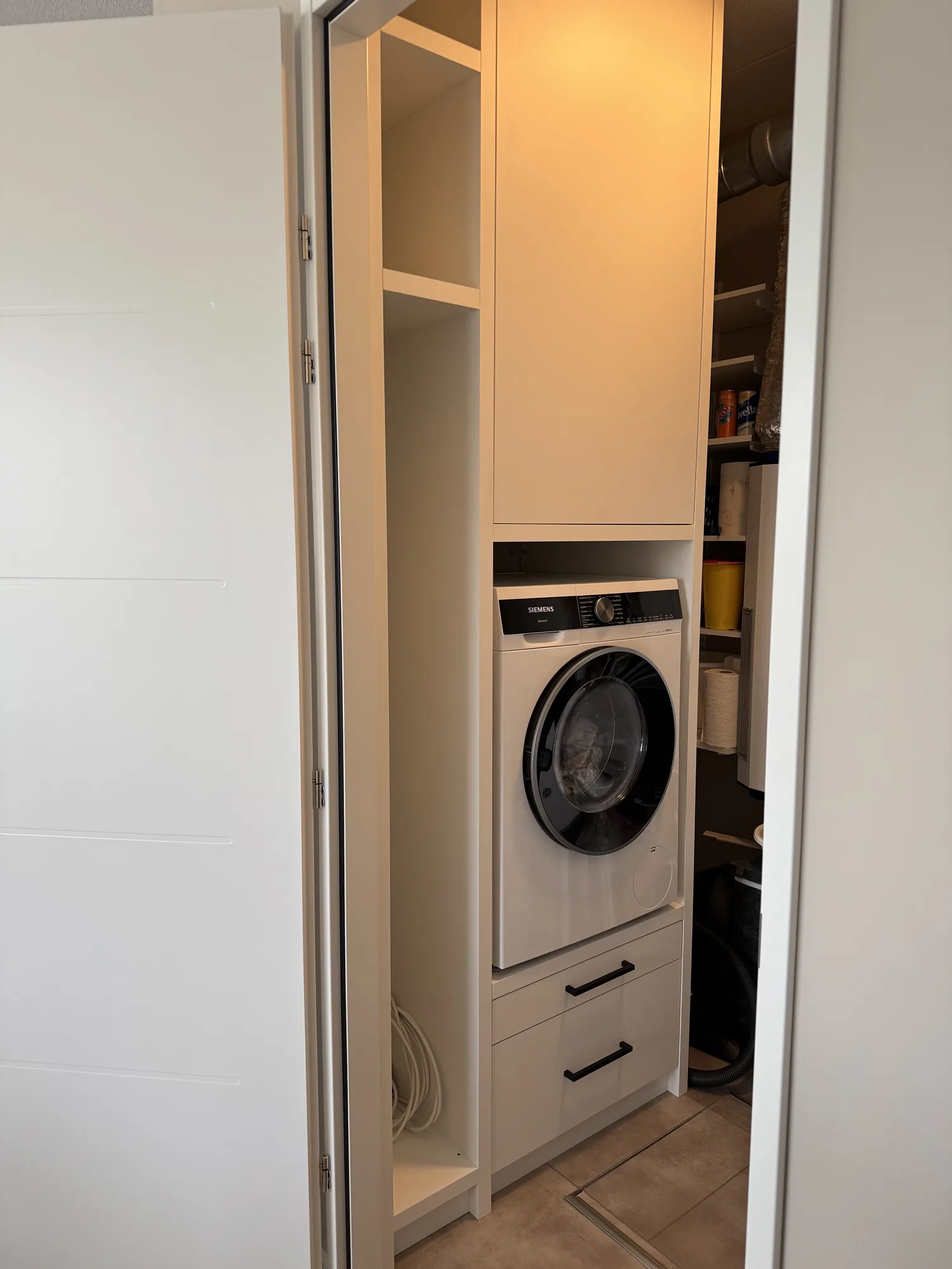 Wasmachinekast in een halkast, met de wasmachine op een ladenblok en schappen erboven