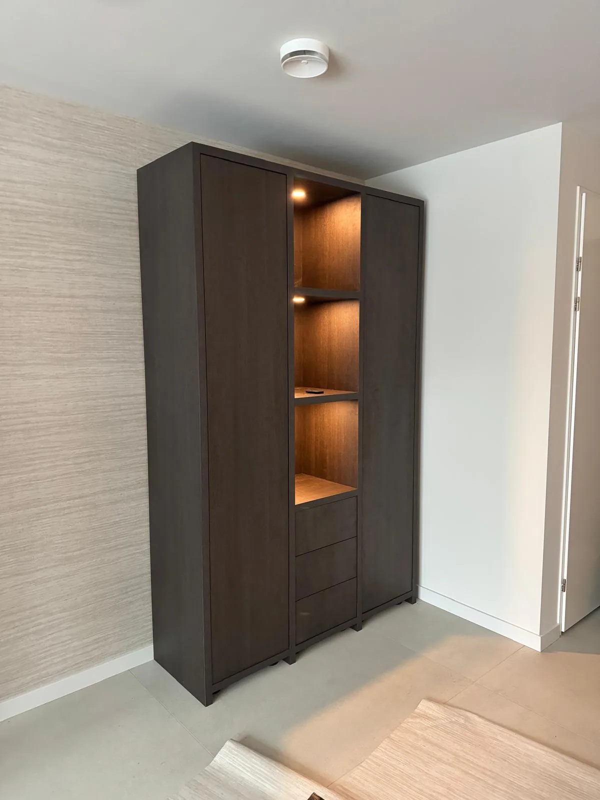 Kast in donker eiken met verlichte open vakken en laden, in een hal