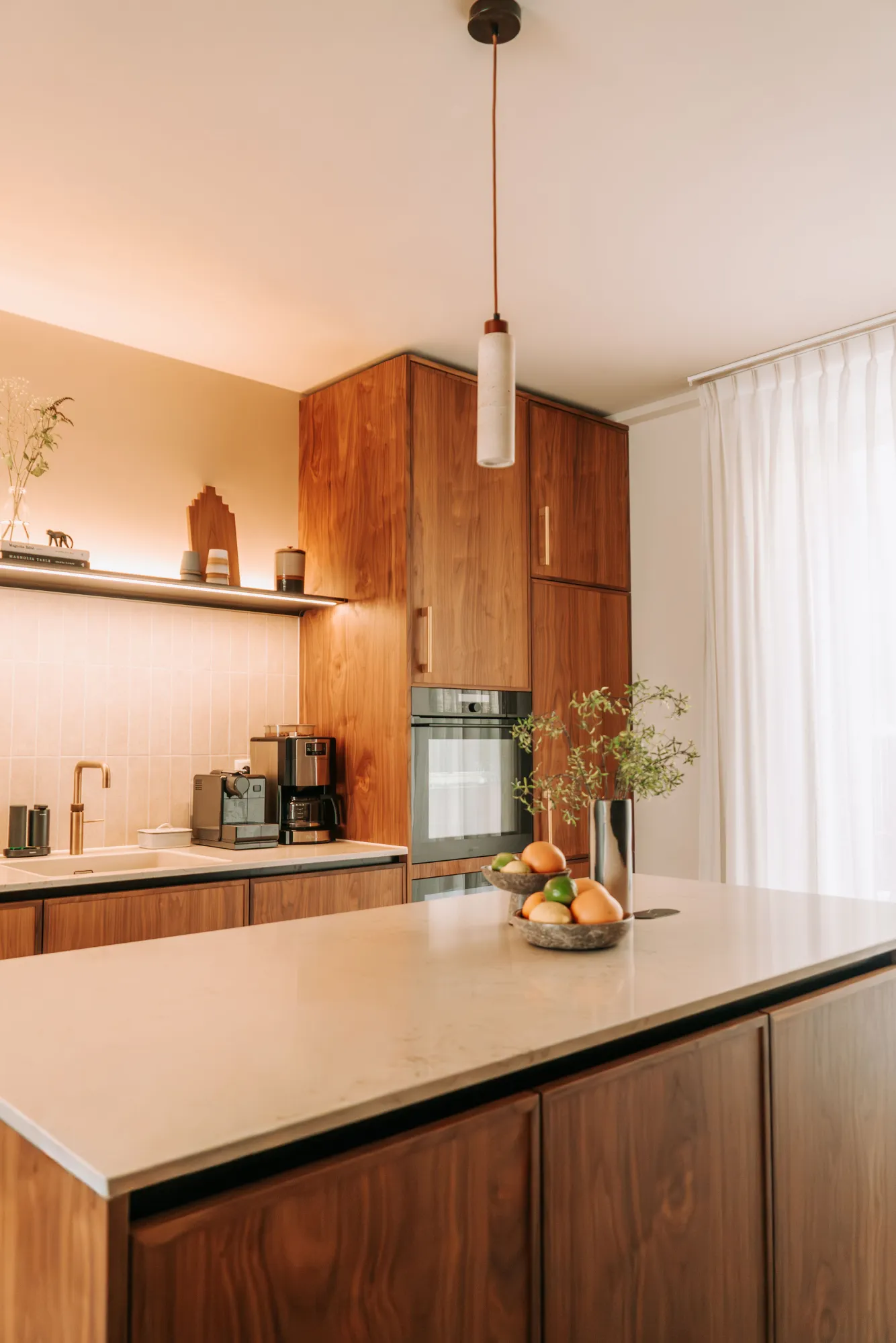 Kookeiland met een stenen blad, met daarachter de hoge kasten in noten met ingebouwde oven