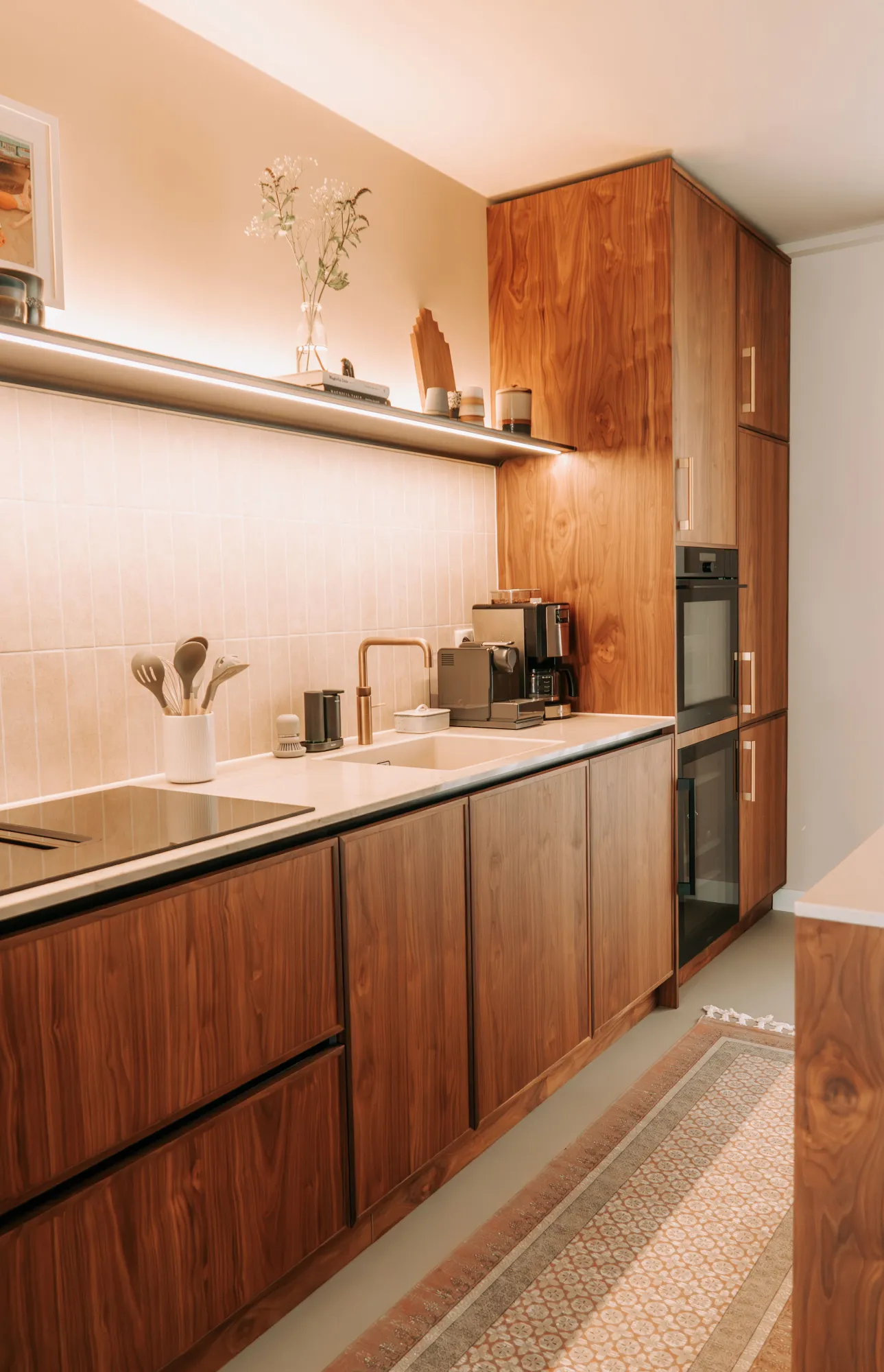 Keukenwand in noten met kookplaat, spoelbak en een hoge kastenwand met oven en wijnkoeler