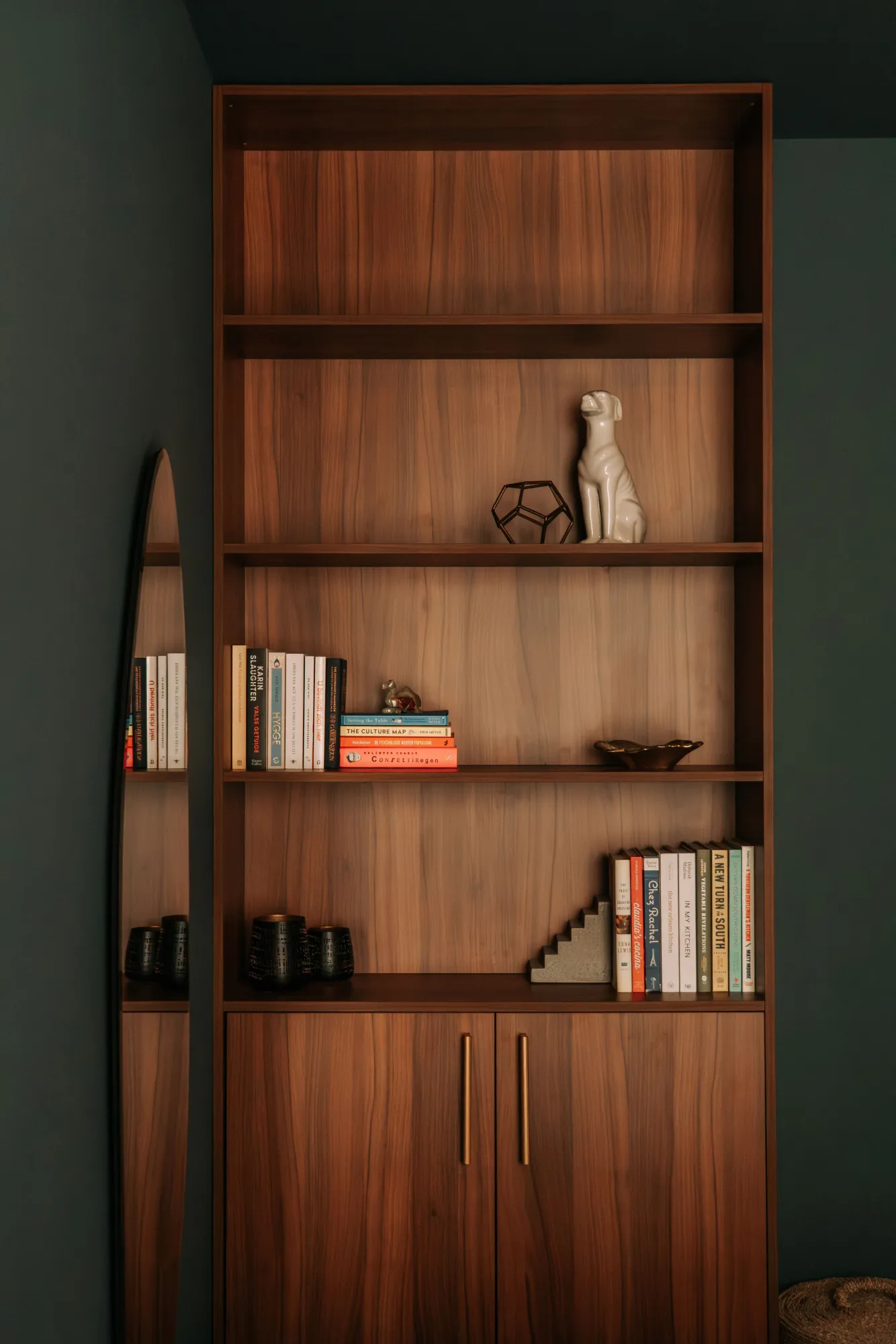 Boekenkast op maat met open vakken boven en gesloten deuren onder, tegen een donkergroene wand