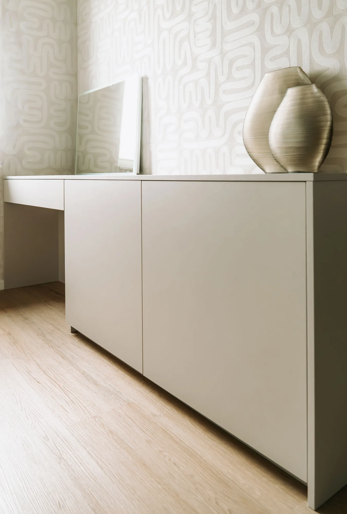 Kaptafel in taupe met een spiegel en een vaas, tegen een wand met patroonbehang