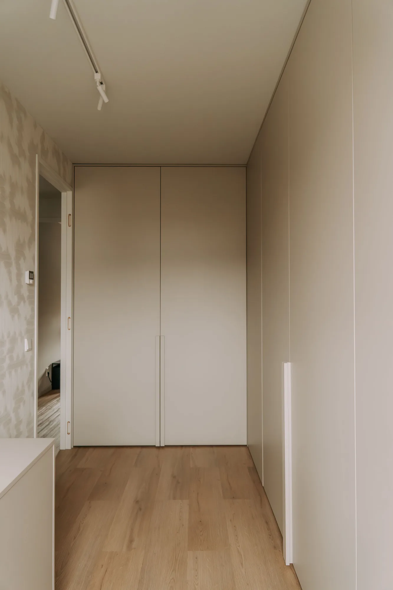 Kastenwand in taupe van vloer tot plafond in een gang, met lange verticale grepen