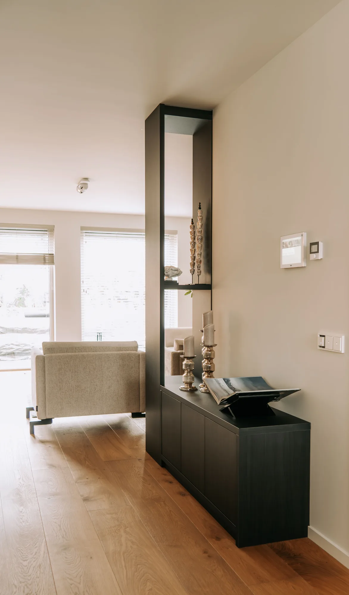 Smalle zwarte roomdivider met een laag dressoir ernaast