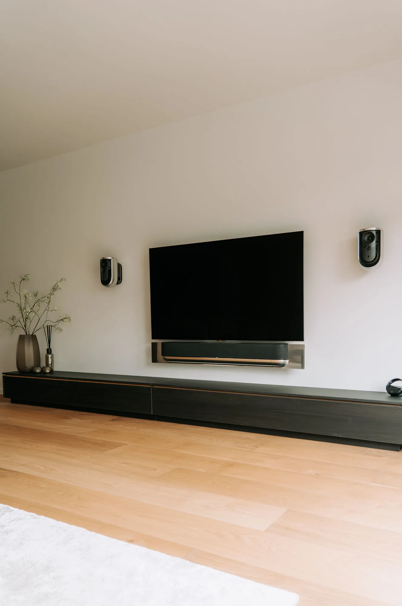 Het zwarte tv-meubel van voren, met de televisie en twee speakers aan de wand